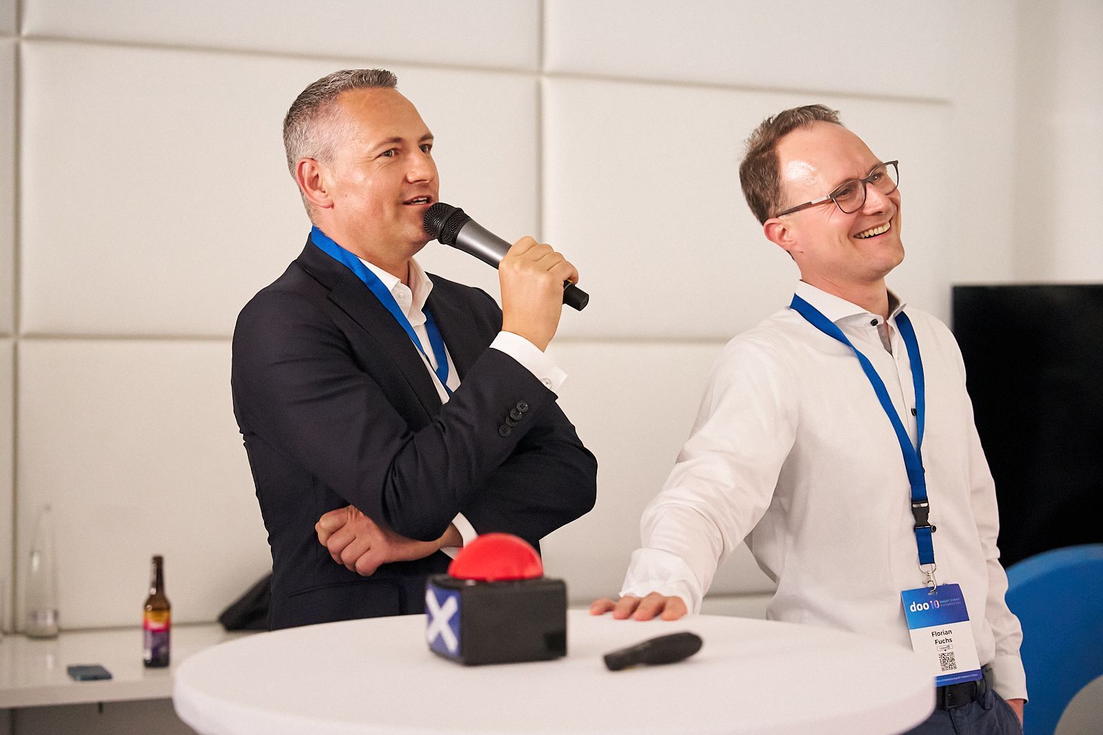 Zwei Männer sitzen an einem Tisch und sprechen in Mikrofone.