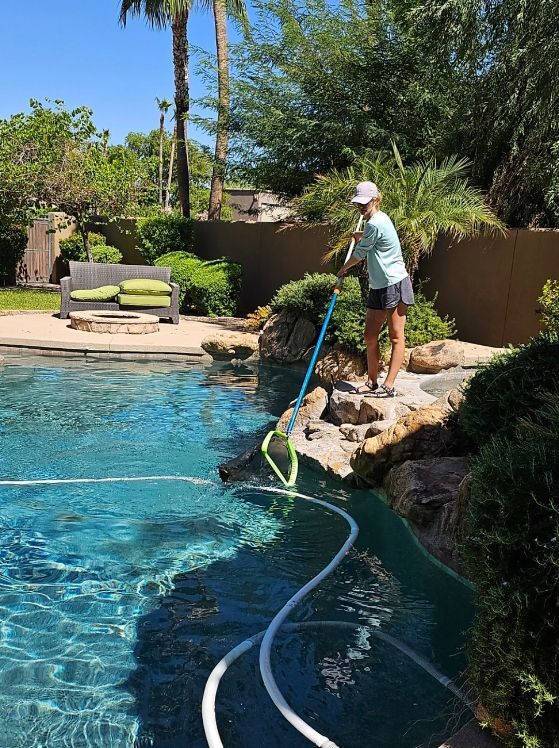Woman cleaning a pool with a net, standing on rocks next to the water.