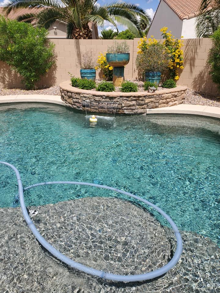 Pool with light blue water and stone wall feature. Blue hose coiled on edge.