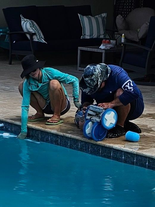 Two people inspecting a robotic pool cleaner at the edge of a blue pool.