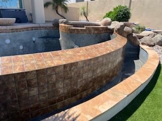 Empty pool with tiled walls and surrounding landscaping.