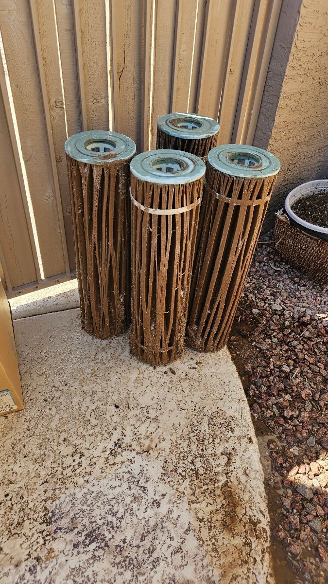 Four cylindrical, brown cactus rib art pieces with metal tops, sitting on gravel.