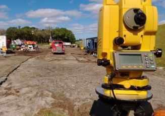 A yellow theodolite is sitting on top of a dirt road.