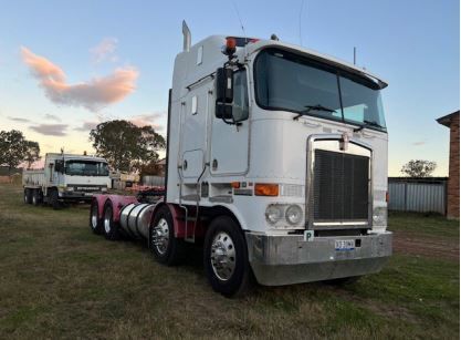 A white semi truck is parked in a grassy field.