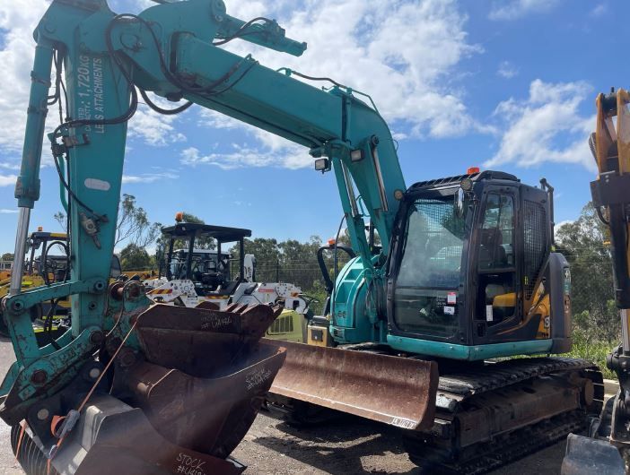 A green excavator is parked next to a yellow excavator in a parking lot.