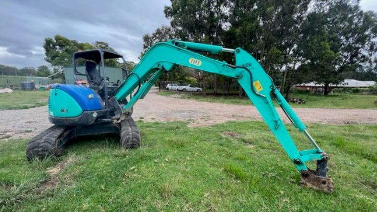 A small blue excavator is sitting on top of a lush green field.