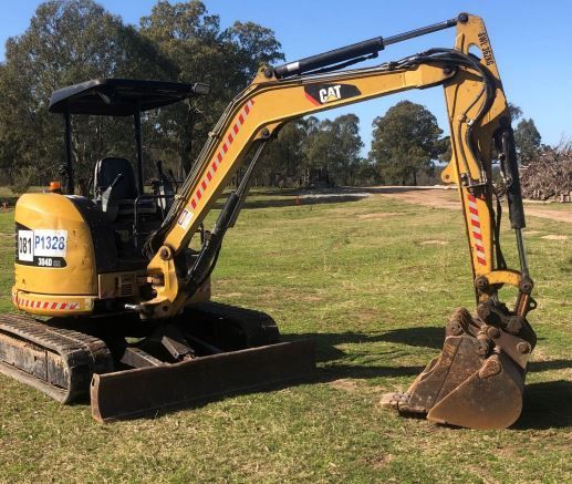 A yellow cat excavator is parked in a grassy field.