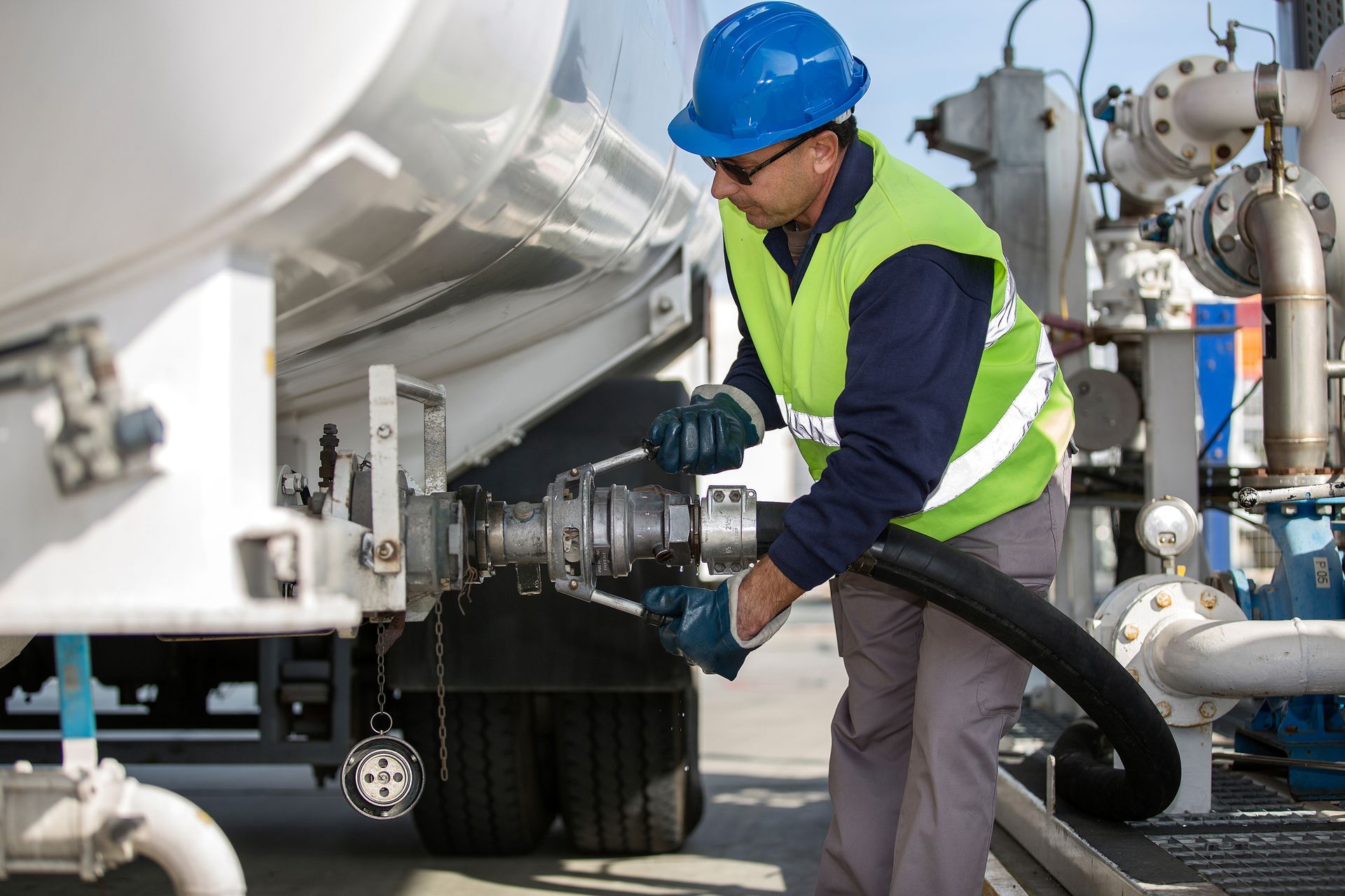 A man wearing a hard hat and safety vest is pumping gas into a truck.
