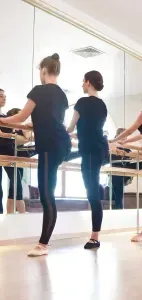 Ballet class in a studio, dancers practicing at the barre in black leotards and tights.
