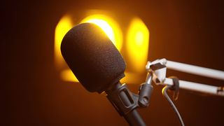 Microphone with foam windscreen on a boom arm, lit by warm yellow studio lights