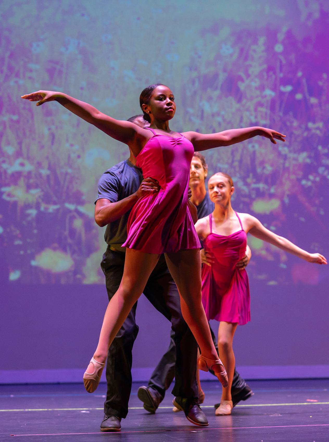 Ballet class in a studio, dancers practicing at the barre in black leotards and tights.