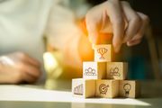 Hand placing glowing block on stacked cubes with business icons, in a soft-lit workspace
