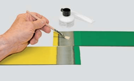 Hand applying glue to join yellow and green strips. Bottle and applicator nearby.