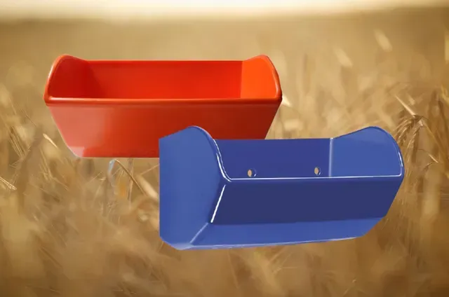 Red and blue plastic feeding troughs against a blurred wheat field background.