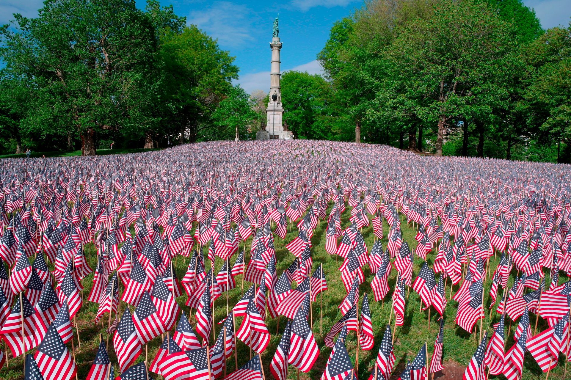 Sea of American flags in a memorial field with a monument and trees under a blue sky