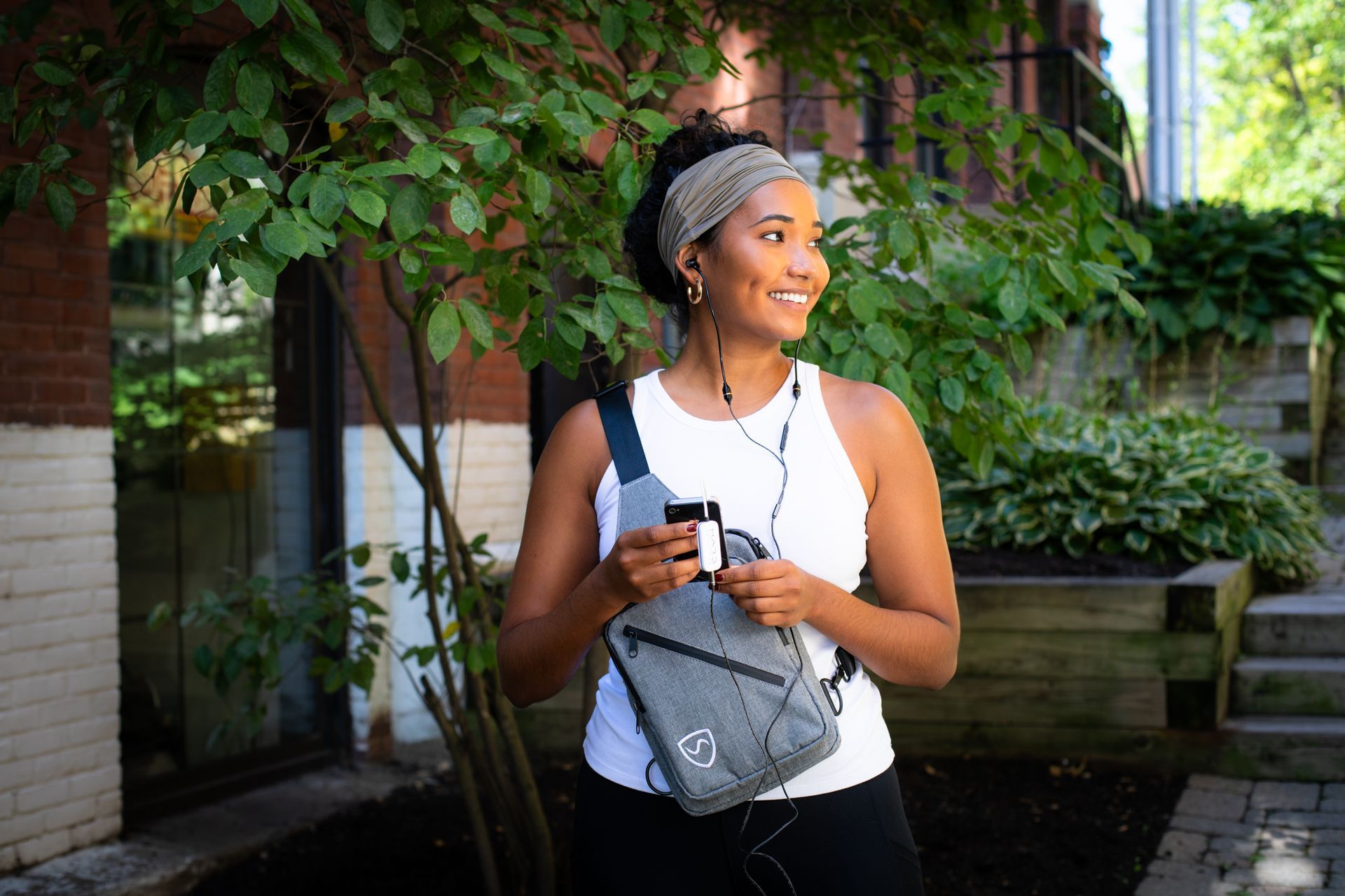 Woman smiling, wearing headphones and holding iPhone while using Shield Your Body products. Lifestyle product photography by JAM Creative, photographers in Burlington Vermont.