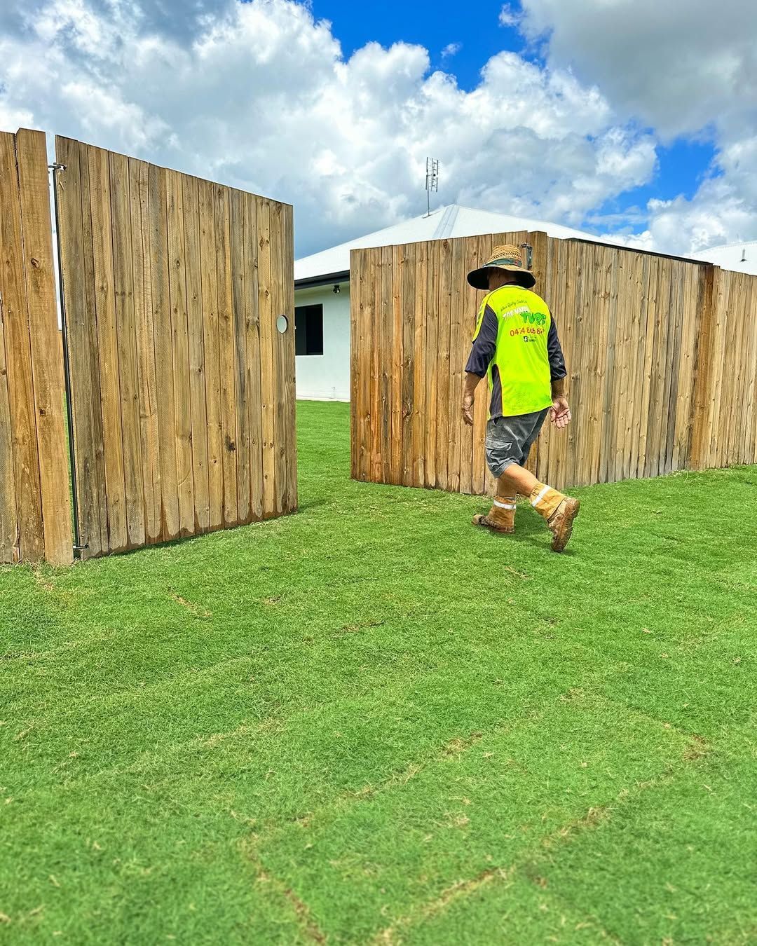 Man in Safety Vest Walking Through Opening in Wooden Fence on Green Lawn — Top Notch Turf in Clermont, QLD