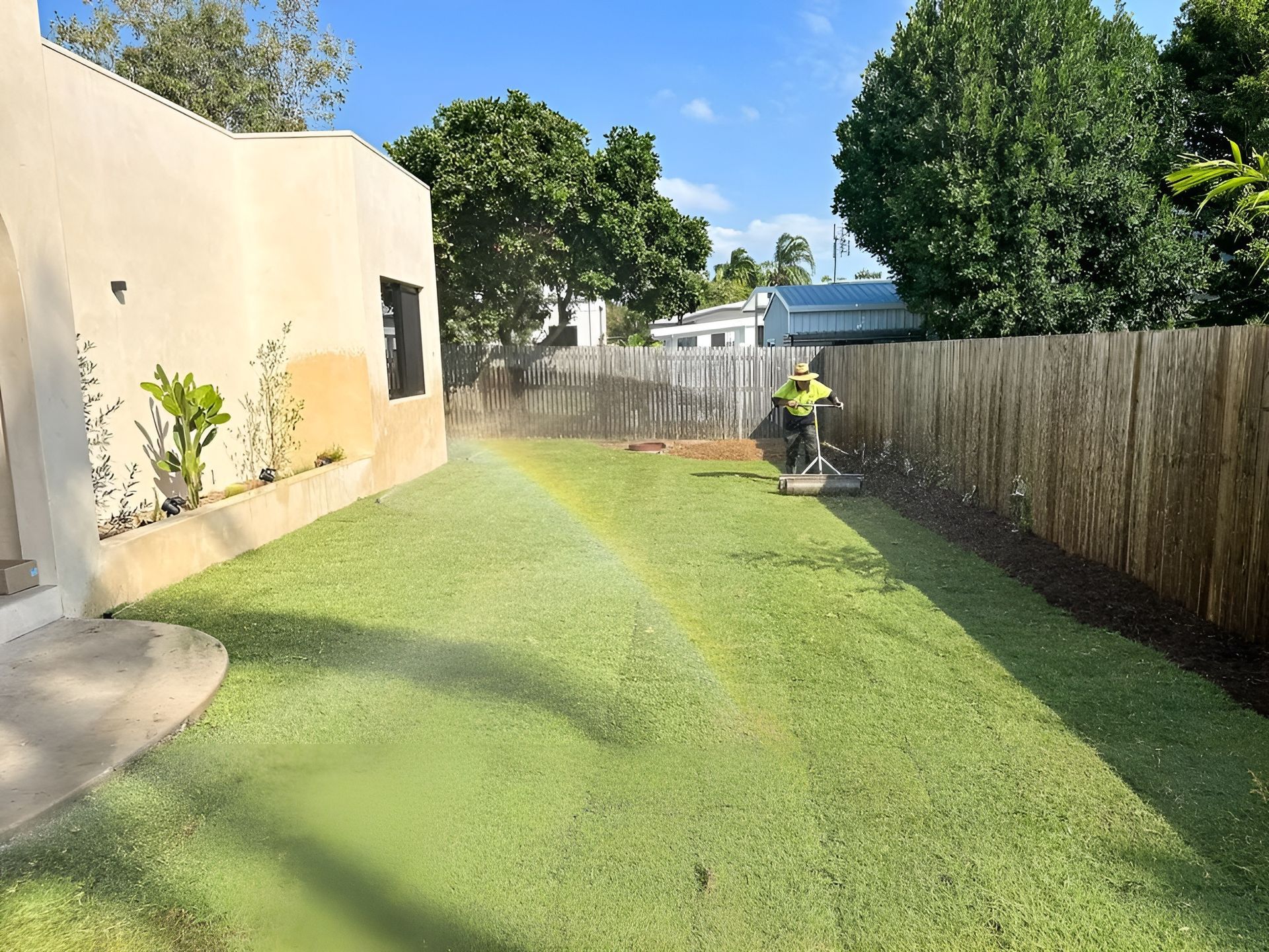 Lawn Being Watered with Sprinkler, Person in Safety Gear Mowing — Top Notch Turf in Winton, QLD