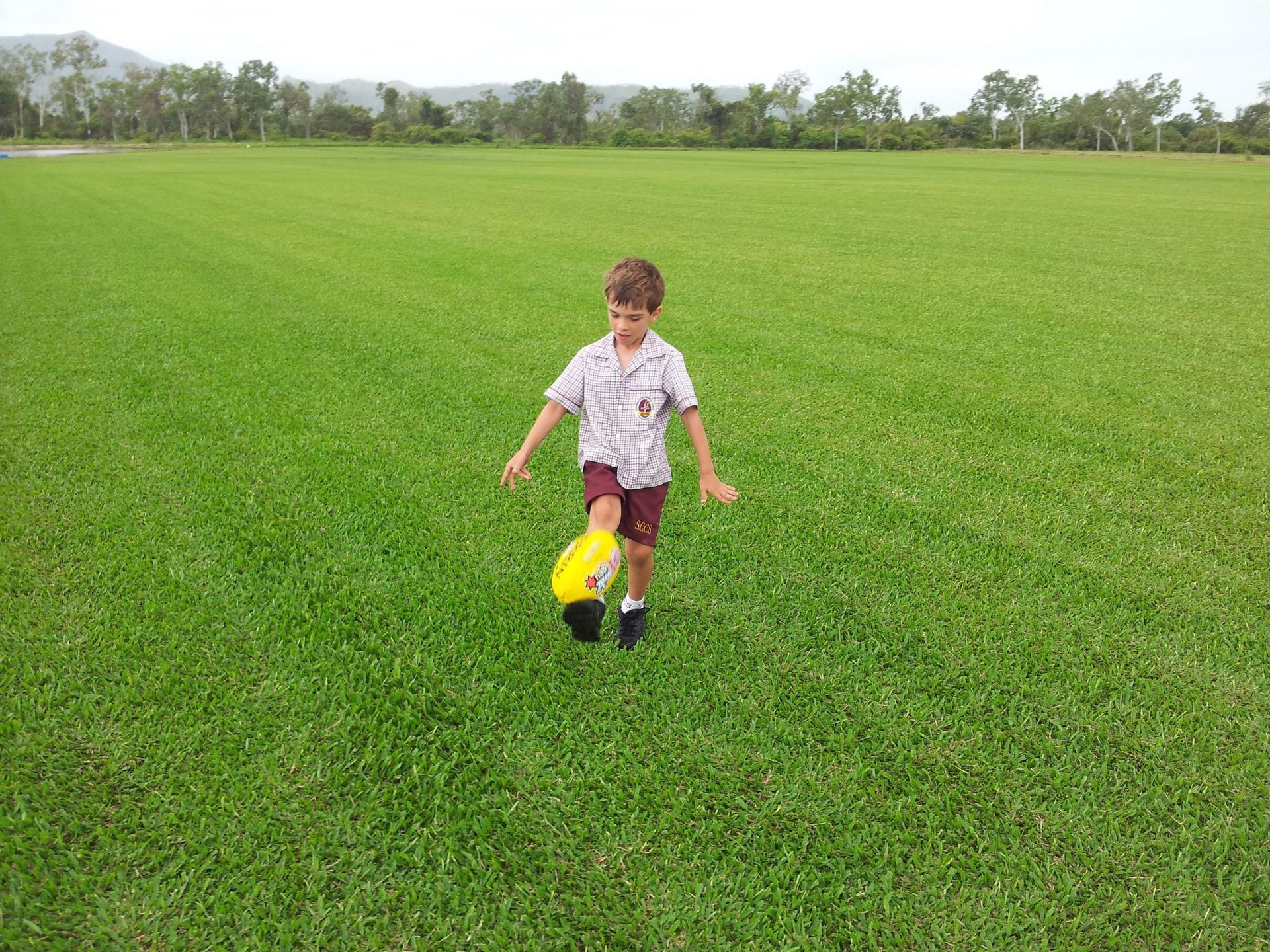 Boy in School Uniform Kicking a Yellow Ball on A Green Grassy Field — Top Notch Turf in Charters Towers, QLD