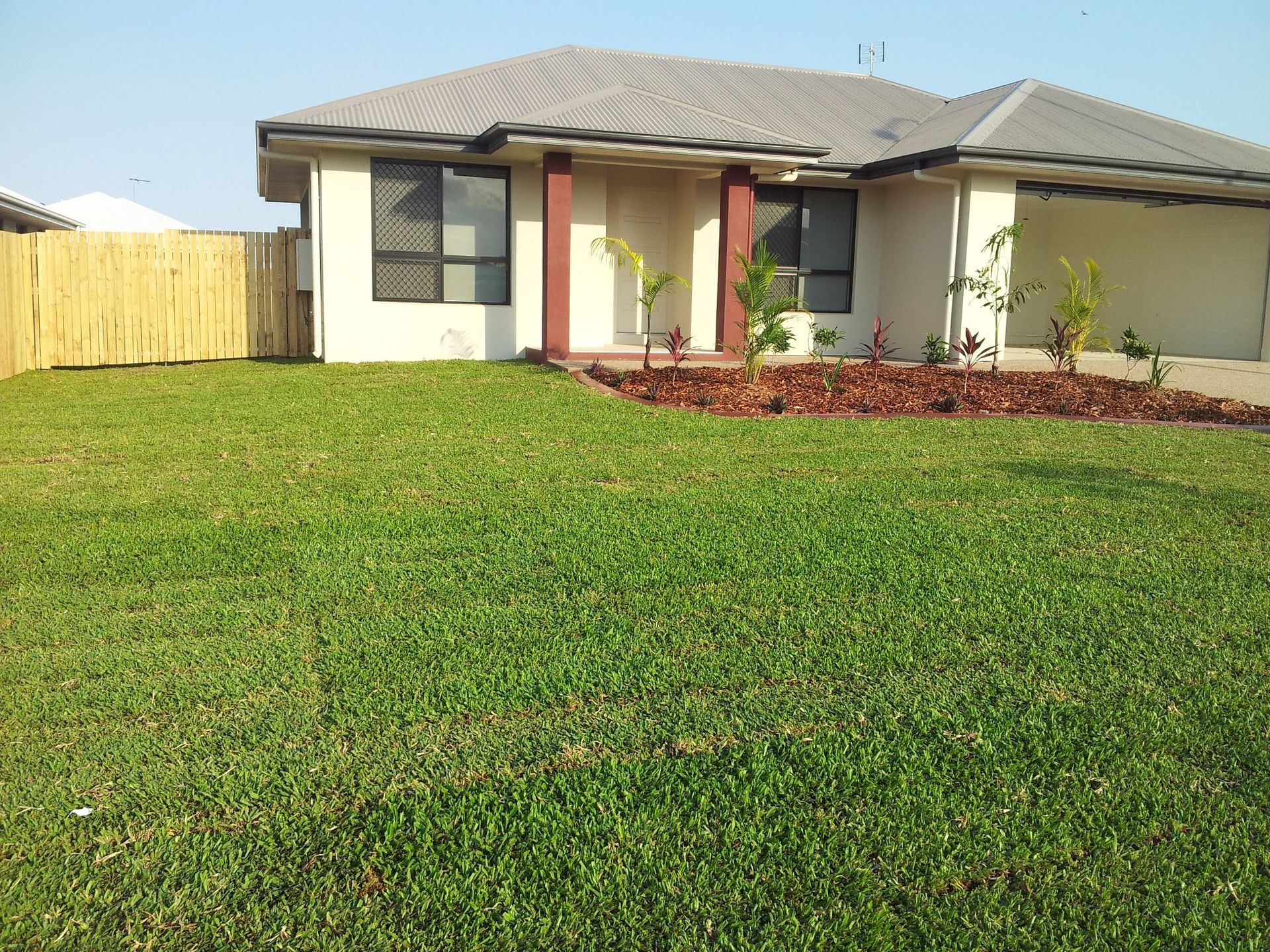 Suburban House with Green Lawn and Wooden Fence, Flower Bed with Brown Mulch — Top Notch Turf in Ingham, QLD