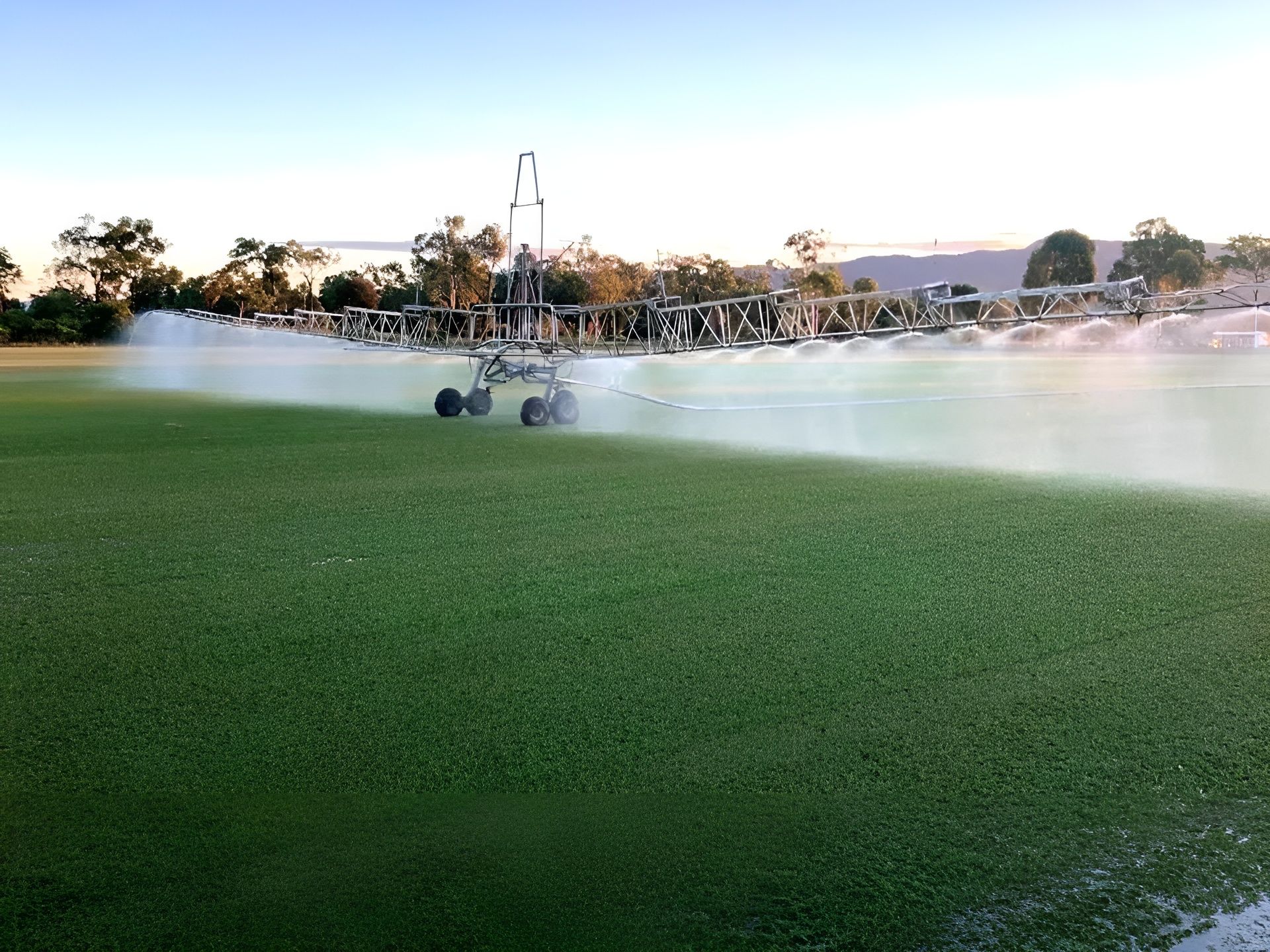 Sprinkler Machine Watering a Green Sports Field. the Sky Is Clear, and The Field Is Lush — Top Notch Turf in Rasmussen, QLD