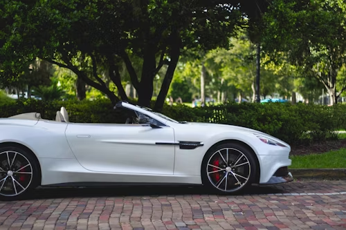 A white convertible sports car is parked on a brick driveway.