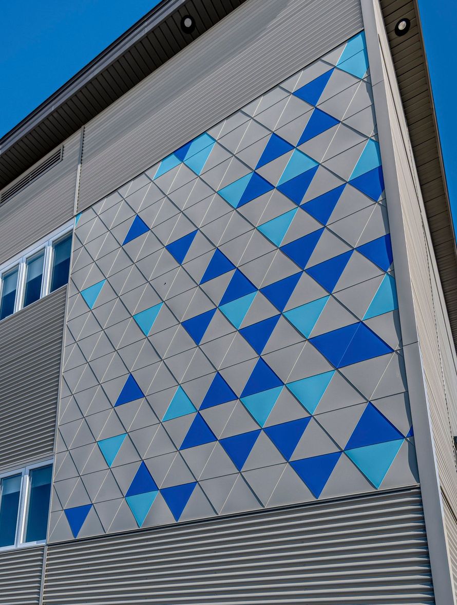 Façade d'un bâtiment moderne présentant un mur d'accent recouvert d'un motif géométrique de triangles gris, bleu clair et bleu marine.