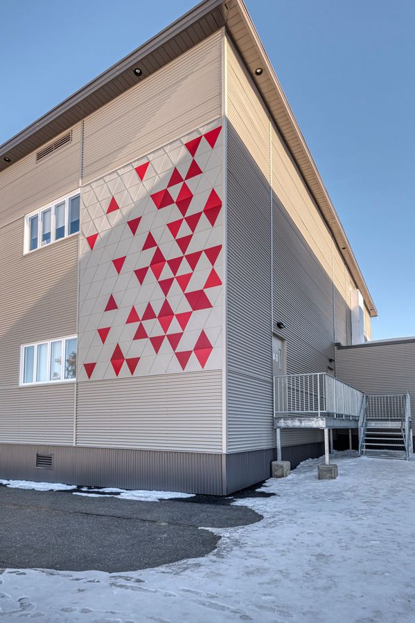 Façade du bâtiment beige avec un motif décoratif de triangles rouges épars sur le mur et un escalier métallique enneigé.
