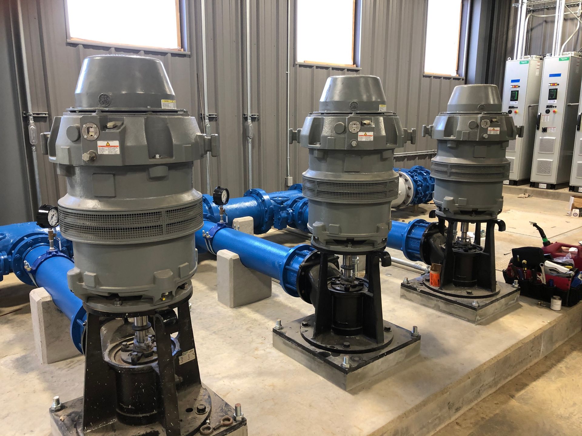 Three water pumps are sitting next to each other in a room with blue pipes.