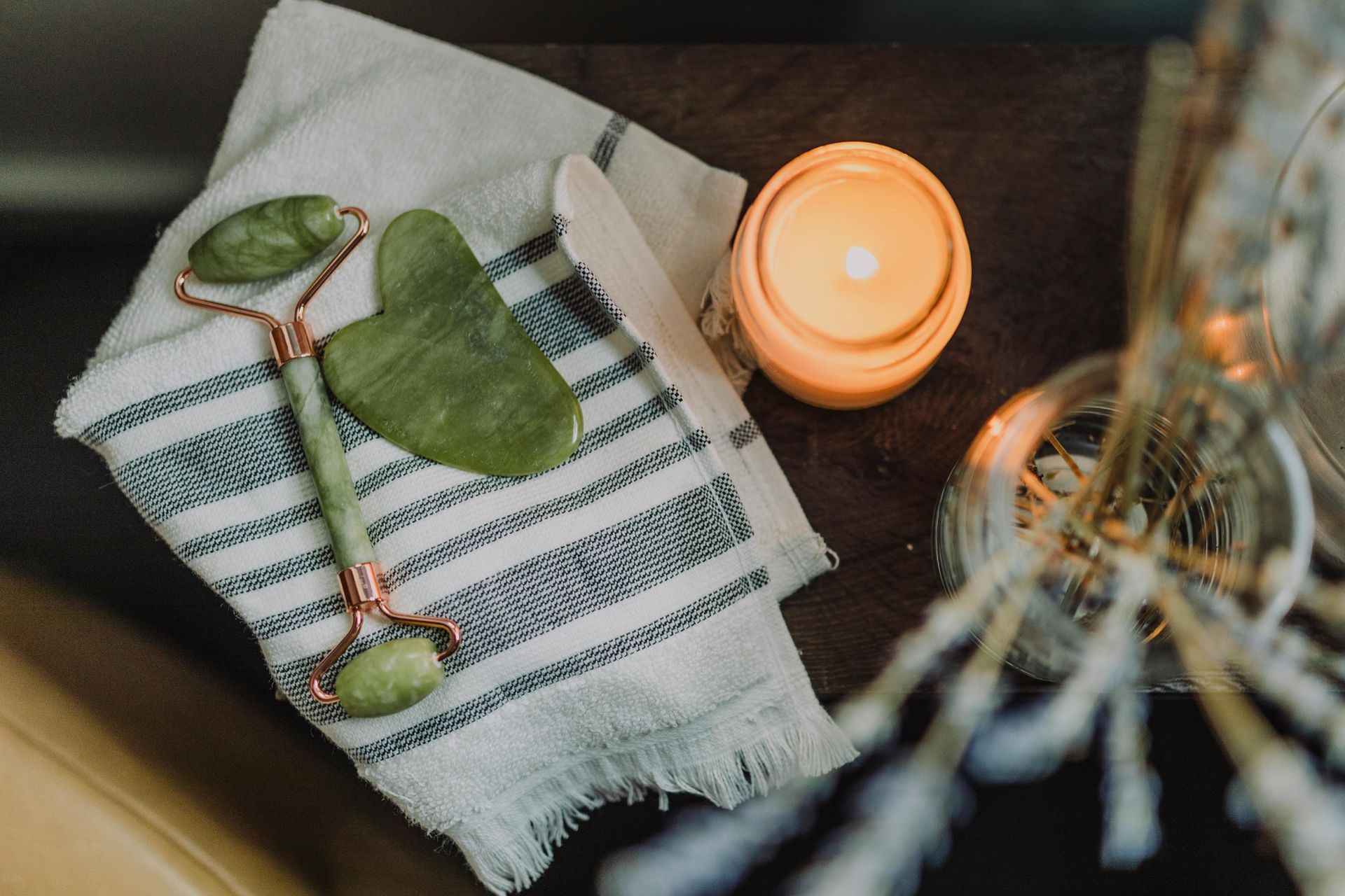 A jade roller is sitting on top of a towel next to a candle.