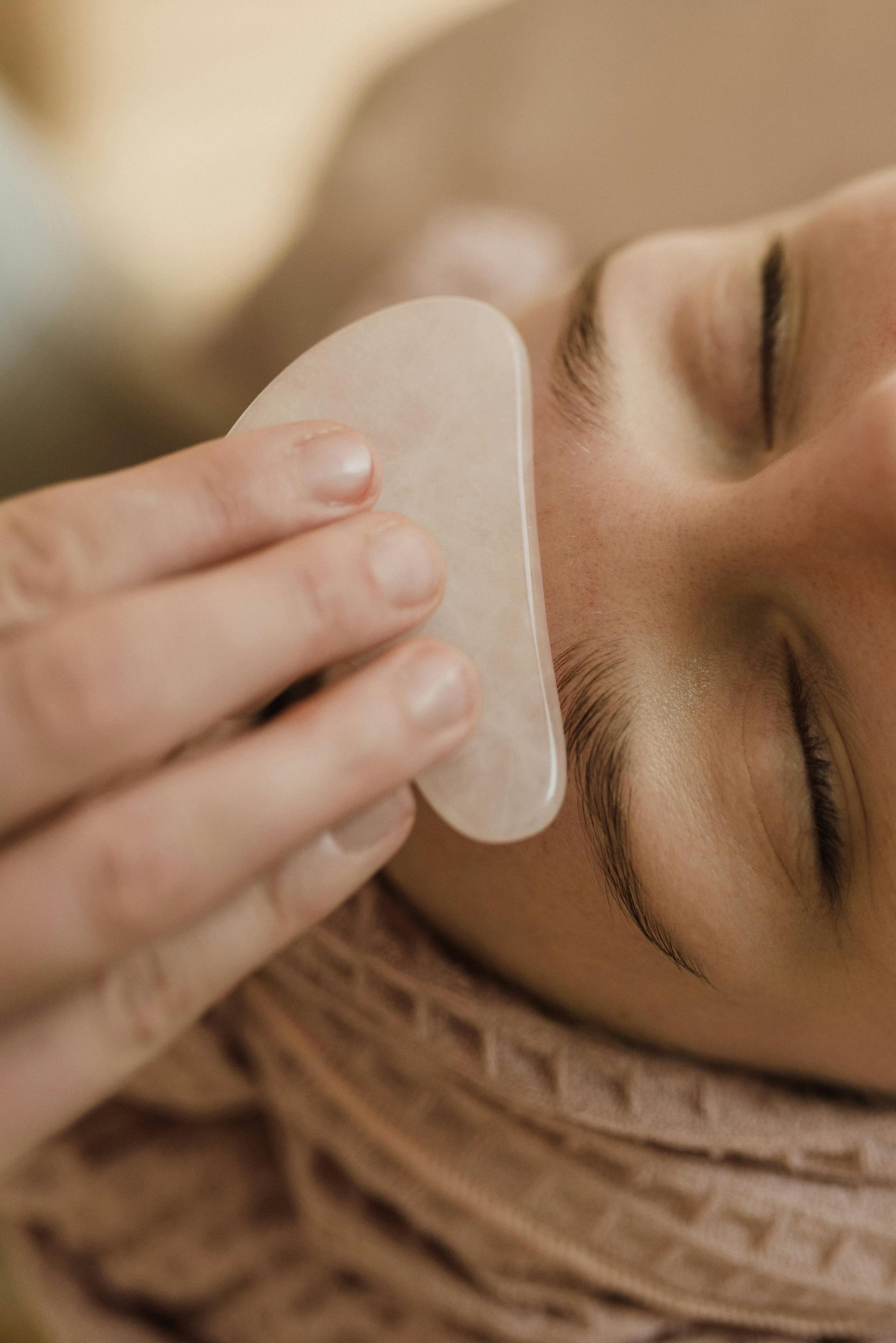 A woman is getting a gua sha treatment on her face.