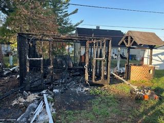 A backyard patio with cobblestone, grass, a large urn with flowers, and a blue trash can.