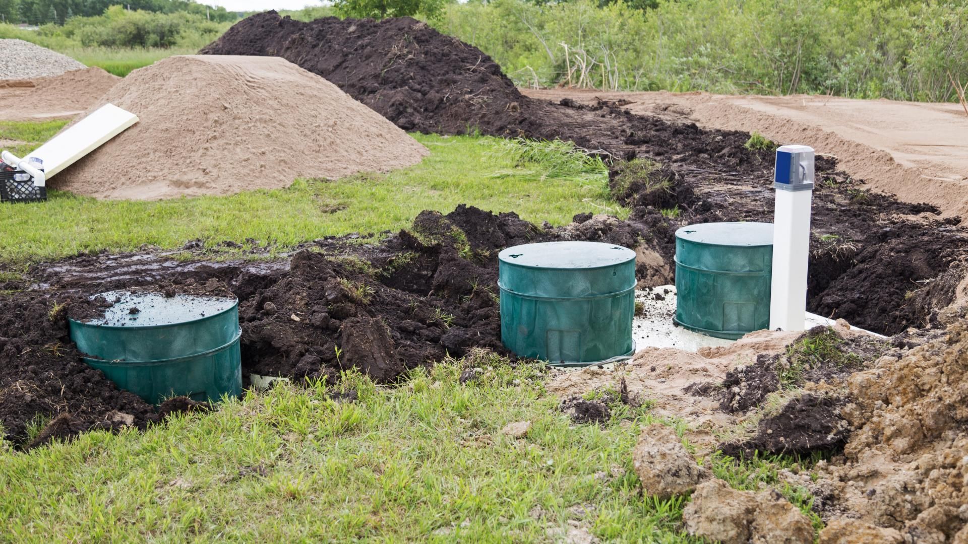 Installation of septic tanks with excavated ground, soil piles, and a white pipe outdoors.