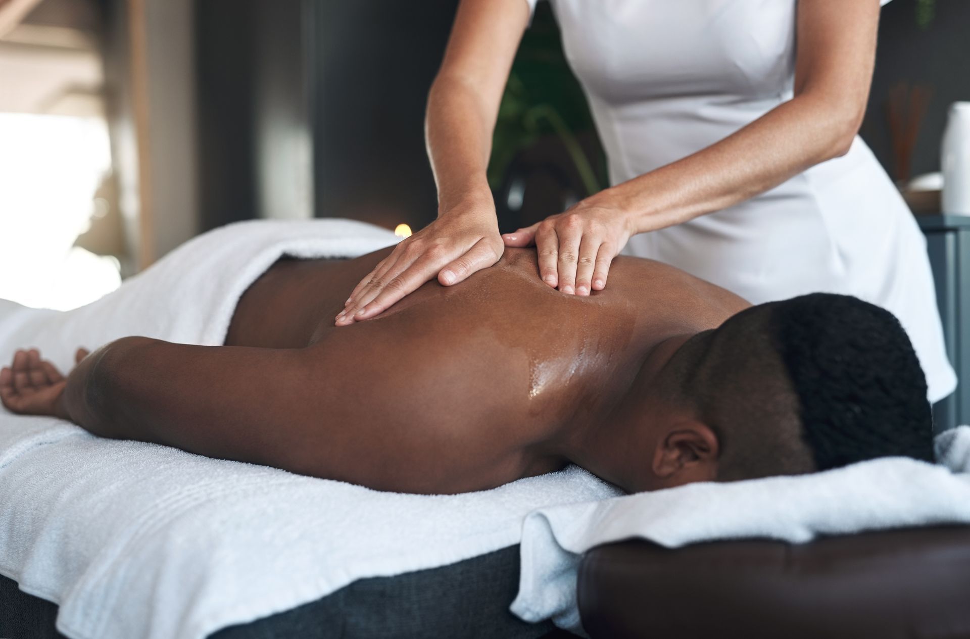 A therapist giving a back massage to a young man lying on a massage bed.