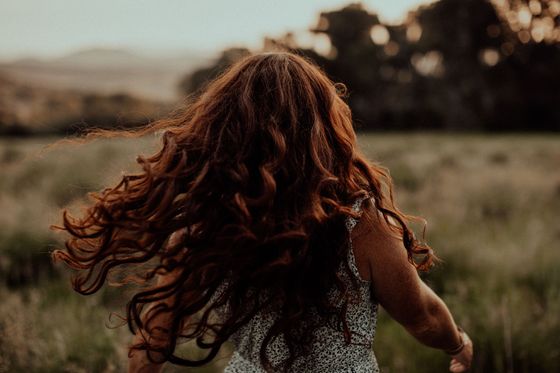 A woman with long red hair is running through a field.