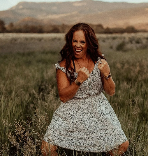 A woman in a white dress is kneeling in a grassy field.