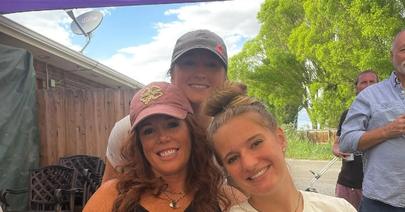 Three women are posing for a picture together in front of a house.