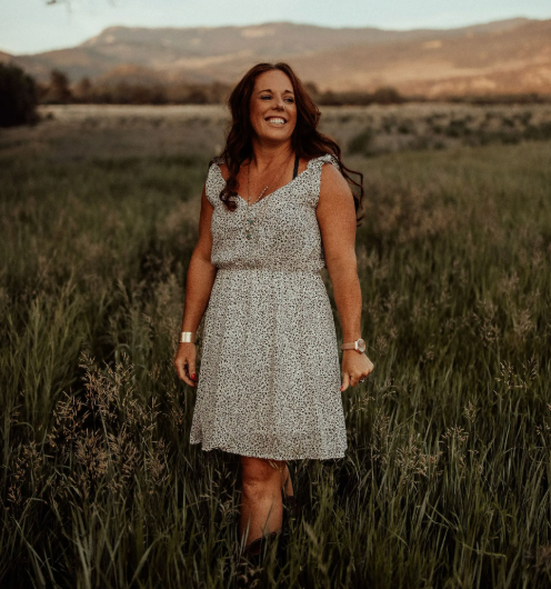 A woman in a white dress is standing in a field of tall grass.