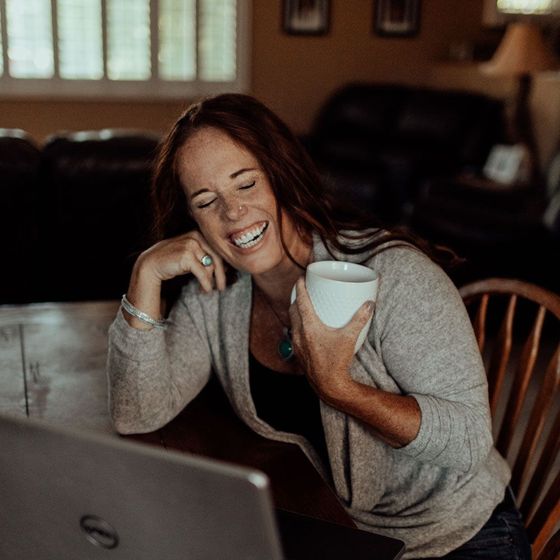 A woman is sitting at a table with a cup of coffee and a laptop.