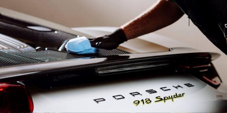 Technician applying ceramic coating to a Porsche 918 Spyder's carbon fiber spoiler, highlighting a glossy, protective finish.