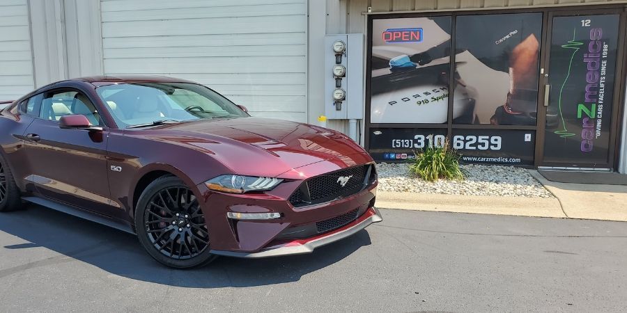 A ceramic coated red ford mustang is parked in front of CarZmedics' shop that did not use a diy ceramic coating kit.