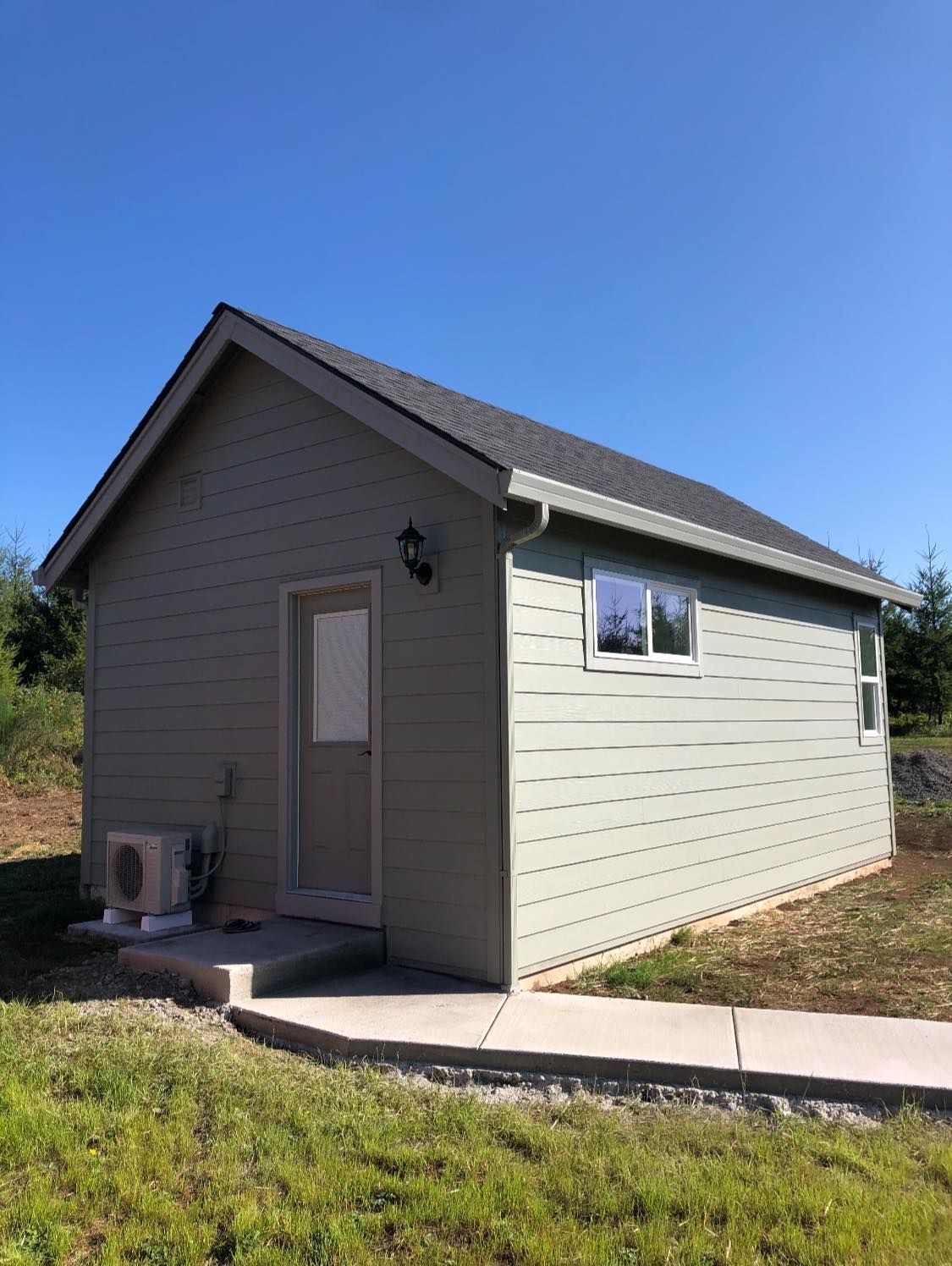 A small house with a gray siding and a gray roof is sitting in the middle of a grassy field.