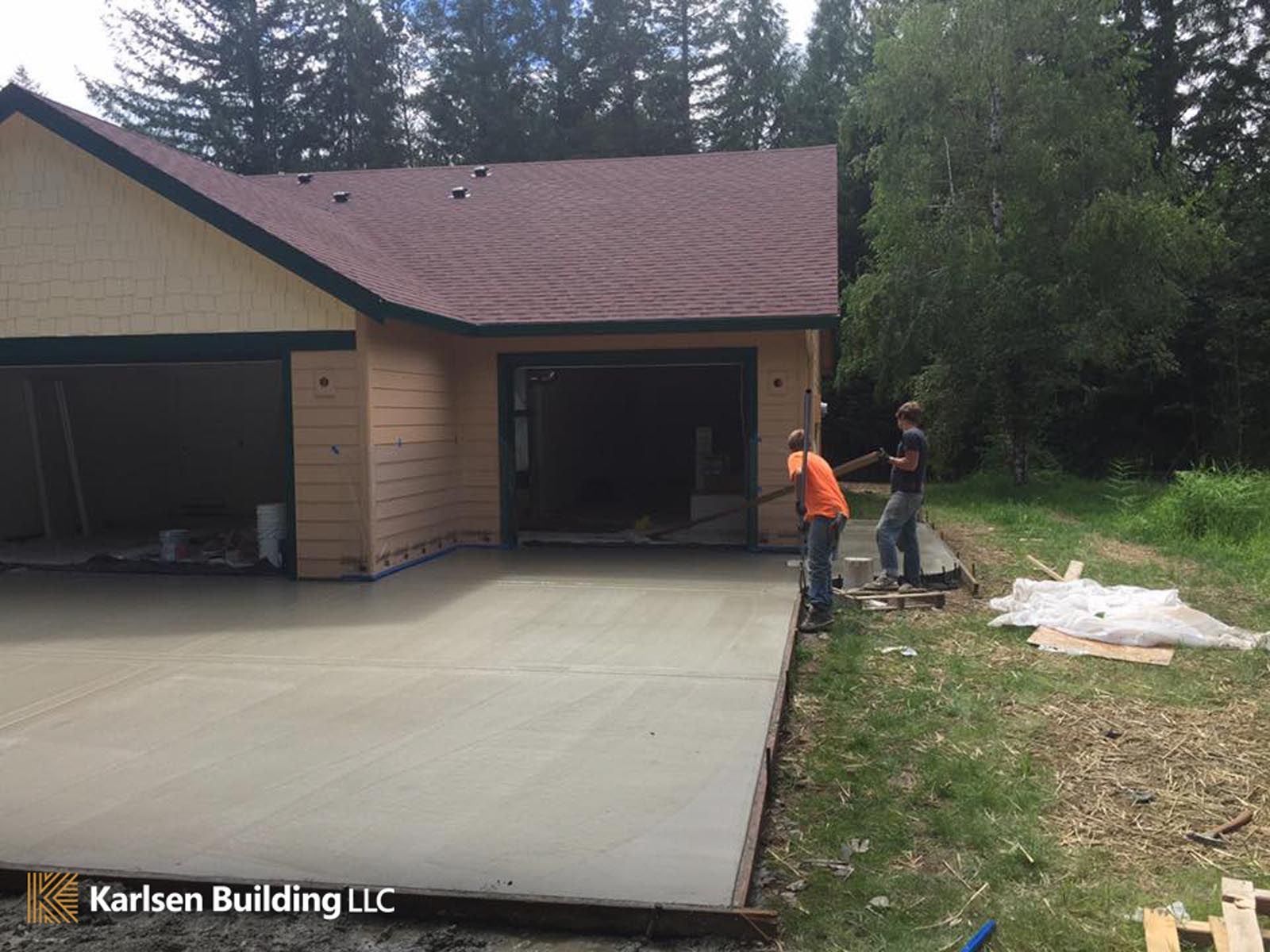 Two men are working on a concrete driveway in front of a house.