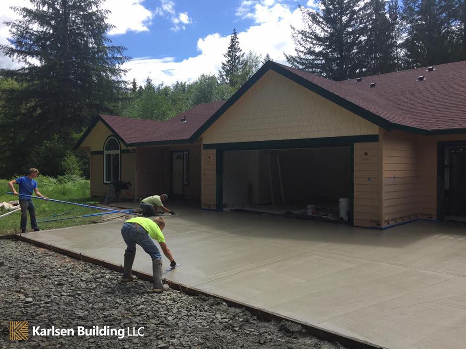 Two men are working on a concrete driveway in front of a house that is being built by karlsen building llc