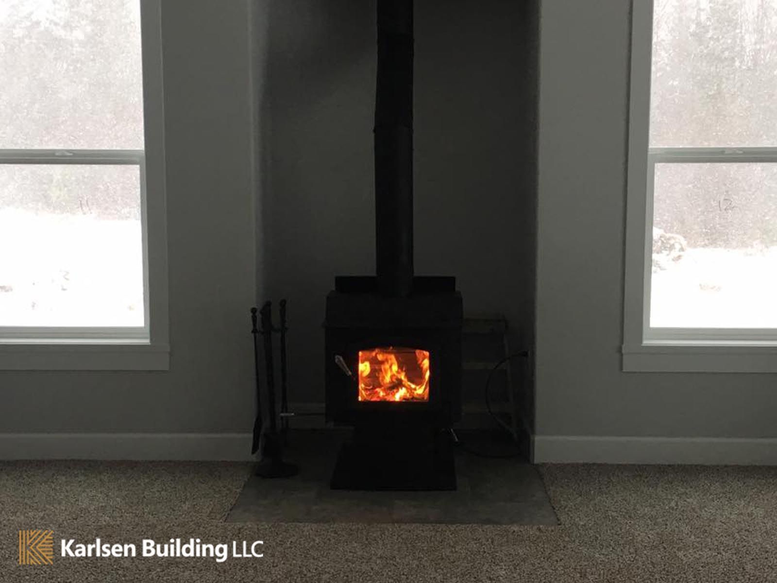 A wood stove is sitting in the corner of a room next to two windows.