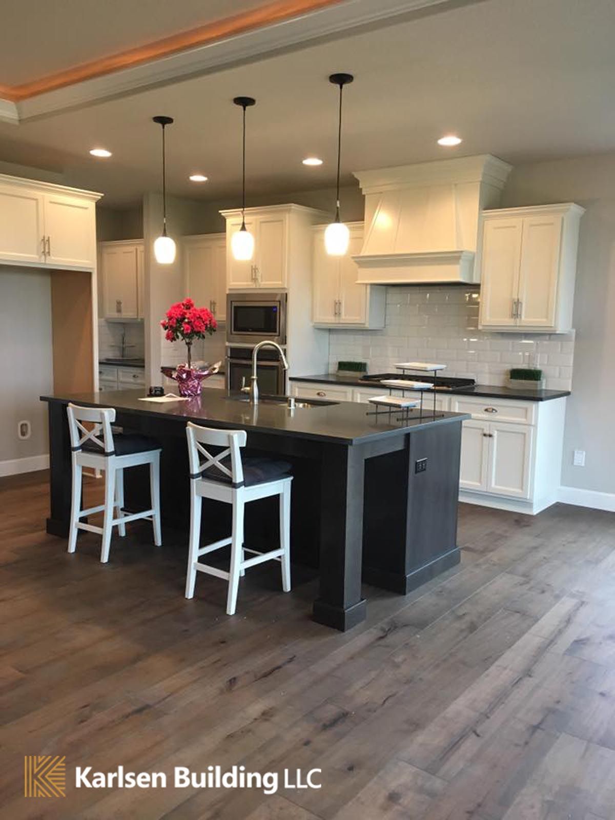 A kitchen with a large island and stools by karlsen building llc