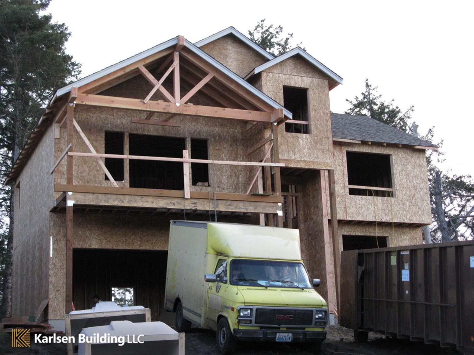 A yellow van is parked in front of a house under construction by karlsen building llc