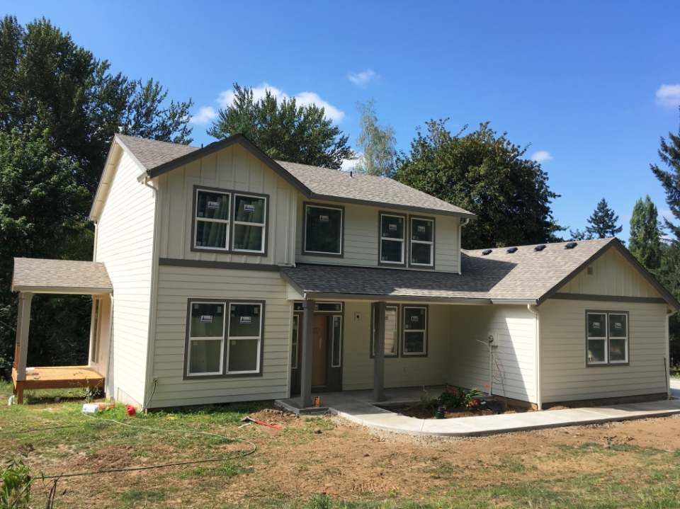 A large white house with a gray roof is sitting on top of a lush green field.