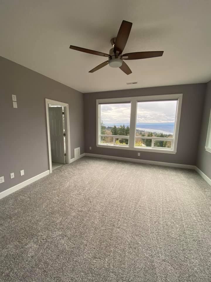 An empty bedroom with a ceiling fan and two windows.