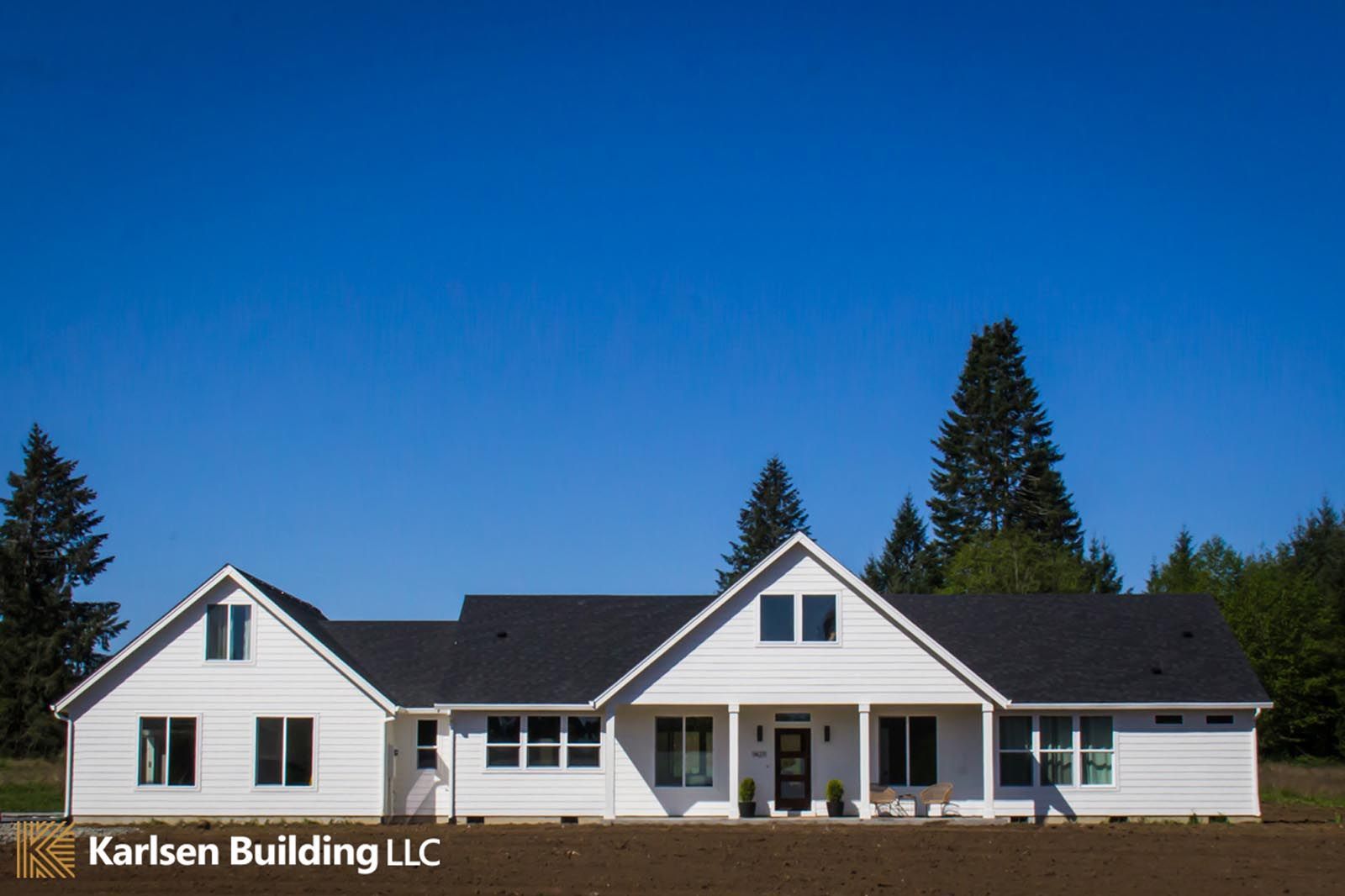 A large white house with a black roof is sitting in the middle of a field.